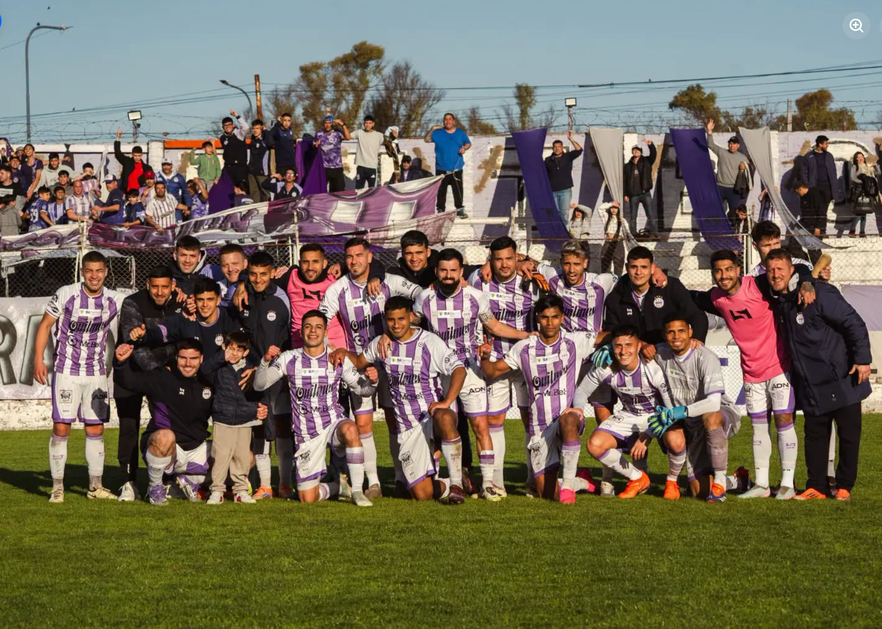 A lower-league Argentine squad posing for a team photo in front of a modest terrace